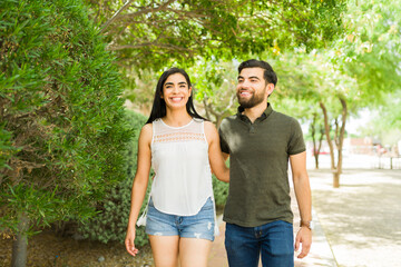 Smiling young hispanic couple happily strolling hand in hand on a sunny day in a beautiful outdoor environment