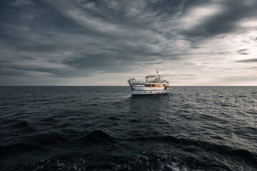 A lone boat sailing on the Adriatic Sea under a dramatic sky near Croatia. The vast expanse of water and the stormy clouds create a captivating seascape.