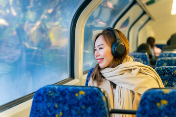Asian woman using mobile phone and listening to music or podcast on headphones during travel on...