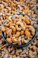 Spicy Seasoned Cashews in a Decorative Bowl, Close-Up View, Close-up of seasoned, spicy cashew nuts in a decorative ceramic bowl, surrounded by a bulk of plain cashews. Ideal for snack and food themes