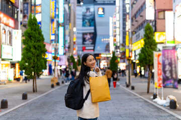 Happy Asian woman holding shopping bag walking at Shibuya district, Tokyo, Japan in evening....