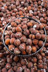 Salted Hazelnuts in Black Bowl Over Scattered Nuts Background, Close-up of salted hazelnuts in a decorative black bowl, set against a backdrop of scattered nuts.