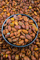 Seasoned Almonds in a Decorative Bowl Close-Up View, Close-up image of seasoned thyme almonds in a decorative enamel bowl, with a blurred background of more almonds.