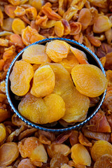 Bowl of Dried Apricots on a Pile of Apricot Halves, Close-up of a colorful bowl filled with succulent dried apricots, surrounded by a textured backdrop of dried apricot halves.