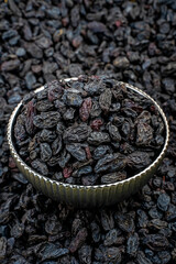 Black Raisins in Silver Bowl on Raisin Background, Close-up of black raisins piled in a silver textured bowl, set against a background of scattered raisins. Focus on texture and natural sheen.