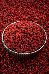 Bowl of Dried Barberries on Textured Red Background, A close-up of a metal bowl filled with dried barberries, set against a vibrant backdrop of similar barberries.