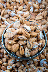 Fresh Salted Almonds in a Bowl Over a Pile, Top View, Close-up view of fresh almonds in a decorative bowl, set against a background of loose almonds. Perfect for health and nutrition themes.