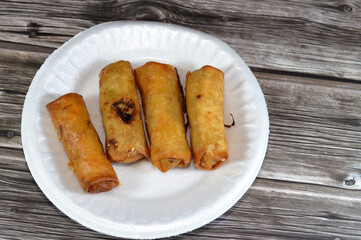 Chinese food cuisine recipe of spring rolls stuffed and filled with chicken pieces and slices of onions fried in deep oil, served in a white plate and on wooden background, selective focus
