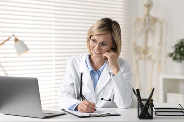 Smiling doctor with laptop having online consultation at table in office