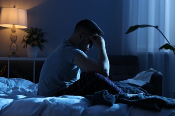 Frustrated man sitting on bed at night