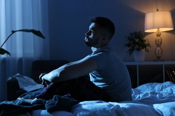 Fototapeta premium Frustrated man sitting on bed at night