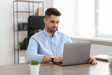 Fototapeta premium Happy young programmer working with laptop in office