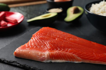Fresh salmon for sushi and other ingredients on dark table, closeup