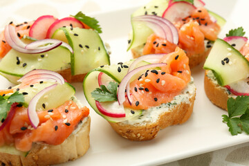 Tasty canapes with salmon served on white wooden table, closeup