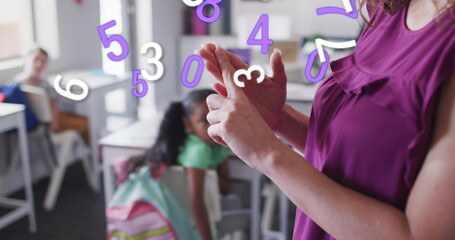 Image of numbers moving over happy biracial female teacher explaining to diverse school class