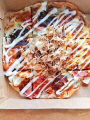 Typical Japanese street snack, Okonomiyaki in a packaging box. Okonomiyaki is made from wheat flour containing vegetables, meat, fish, etc. Then baked on an iron plate and smeared with sauce on top