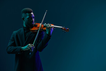Talented young African American man playing violin on dark blue background with copy space