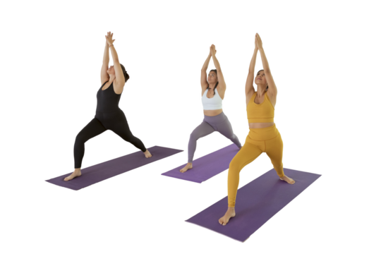 Group of 4 young women doing yoga in a studio, while doing Virabhadrasana 1.