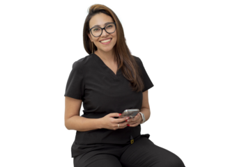 Young female dentist looking at camera smiling, sitting in her office with a cell phone in her hand