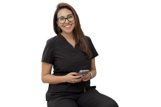 Young female dentist looking at camera smiling, sitting in her office with a cell phone in her hand