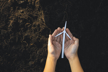 Hand holding wind turbine mockup or model over soil background top view to promote clean...