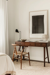 A minimalist Scandinavian-style desk made of walnut wood, placed against the wall of a bedroom interior adorned with black framed art on top.