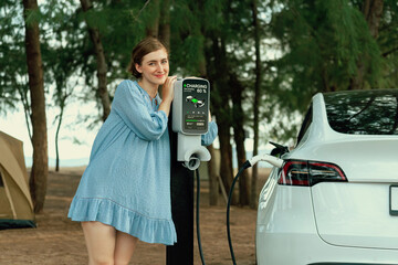Holiday road trip vacation traveling to the beach camp with electric car, young woman recharge EV...