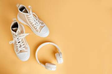 Converse sneakers and white headphones on an isolated orange background. Running and walking shoes....