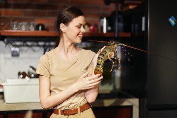 Woman holding fresh lobster in front of black refrigerator in modern kitchen interior