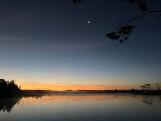 A beautiful sunset over a lake with a moon in the sky © sopaporn