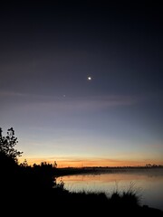 A beautiful sunset over a lake with a large moon in the sky © sopaporn