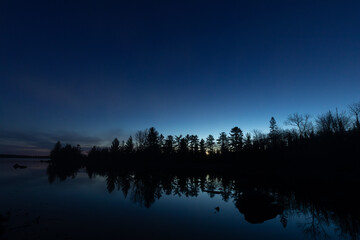 Glow of early morning sunlight illuminates behind the forest for the dawn of a new day