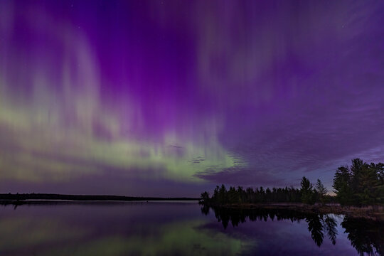 Northern lights erupt over a lake in Minnesota in a dark sky overhead shining rainbow of Aurora light