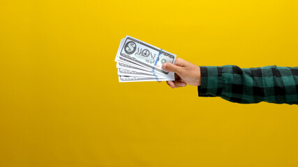 Close-up of a hand holding banknotes against a bright yellow background. Ideal for illustrating concepts of finance, currency, and investment