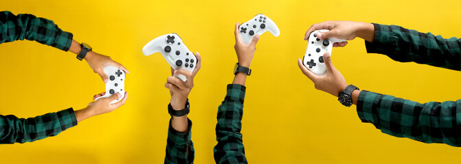 Hand holding a gamepad or joystick against a yellow background with empty copy space for text or...