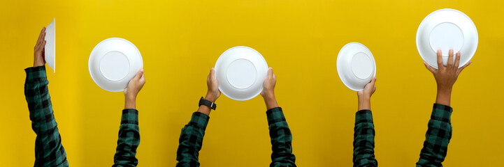 Hand holding empty white plate isolated on a yellow background