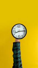 Hand holding a wall clock against a bright yellow background. Ideal for illustrating time management, reminders, or the concept of counting down.