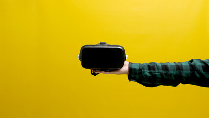 Hand holding a VR headset isolated on a yellow background