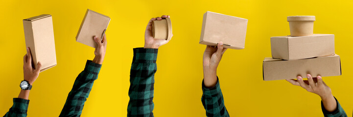 A hand holding a cardboard box against a yellow background, illustrating the concept of shipping,...