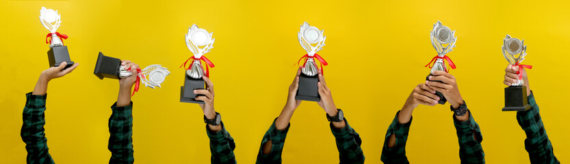 Hand Holding a Silver Champion Trophy, Isolated on a Yellow Background