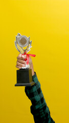 Hand Holding a Silver Champion Trophy, Isolated on a Yellow Background
