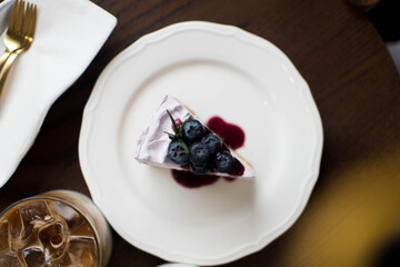 Piece of cheesecake with black currant and blueberry sauce on white plate on wooden table.Horizontal view. top of view..