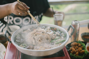 Slice of pork was picking up by the chopstick in the woman's hand above the curved brass pan around with diffused smoke.