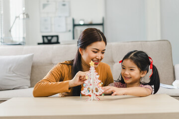 Mother and daughter enjoying crafting a paper christmas tree together at home.