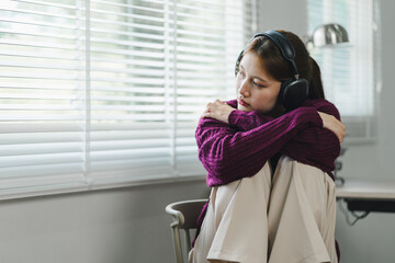 A young woman with headphones sits in a chair, listening intently, focused, and engaged in her...