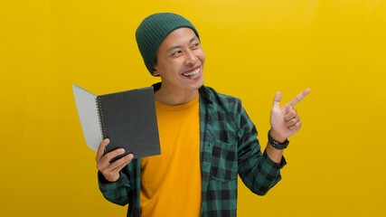 An excited young Asian student, dressed in a beanie hat and casual clothes, is smiling while...