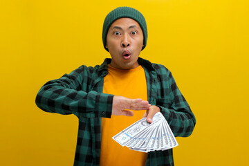 Happy Asian man in a beanie throws banknotes into the air, a joyous expression on his face....