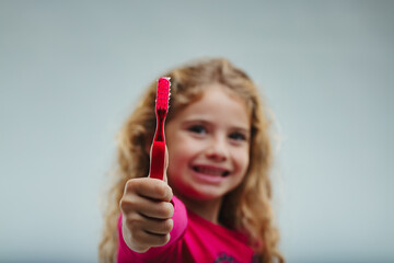 Girl smiles wide, holds red toothbrush up