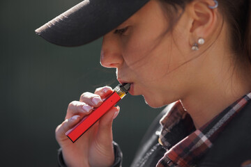 young girl smokes a vape close-up on a dark background, women smoke electronic cigarette in street