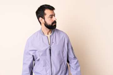 Obraz premium Caucasian man with beard wearing a jacket over isolated background looking to the side